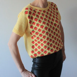 May include: A yellow short-sleeved sweater with a red and green strawberry pattern.