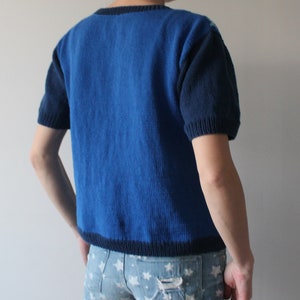 May include: A blue knitted sweater with short sleeves and a dark blue trim. The sweater is made of a soft, comfortable material.