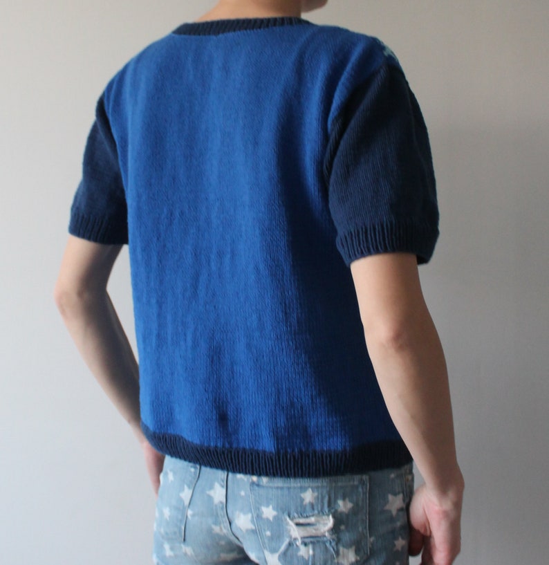 May include: A blue knitted sweater with short sleeves and a dark blue trim. The sweater is made of a soft, comfortable material.