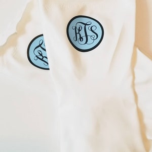 May include: Two white cotton dishcloths with blue and black monogrammed circles. The monogram is the letters "KJS".