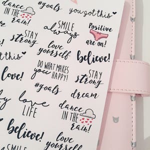 May include: A sheet of stickers with motivational quotes and phrases, including "dance in the rain", "love yourself", "stay strong", "believe", "smile always", "positive are on", "do what makes you happy", "#goals", and "dream".