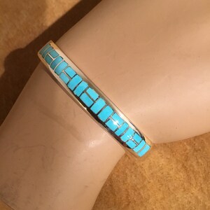 May include: A silver bracelet with a turquoise inlay design. The turquoise is set in a geometric pattern.