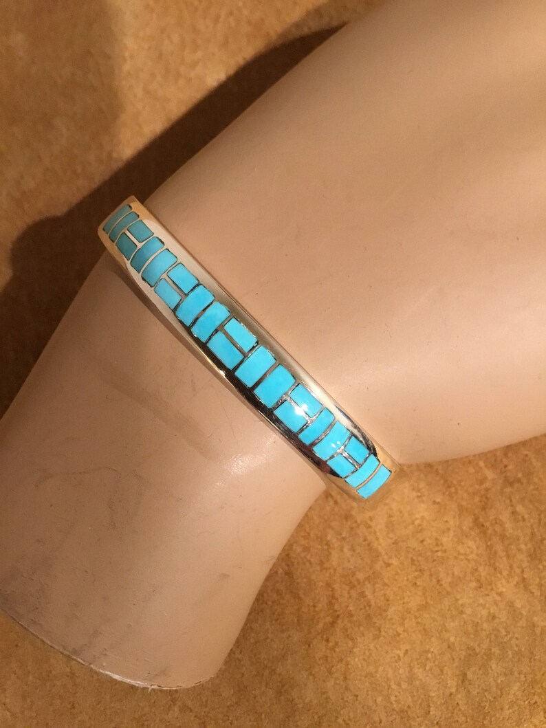 May include: A silver bracelet with a turquoise inlay design. The turquoise is set in a geometric pattern.