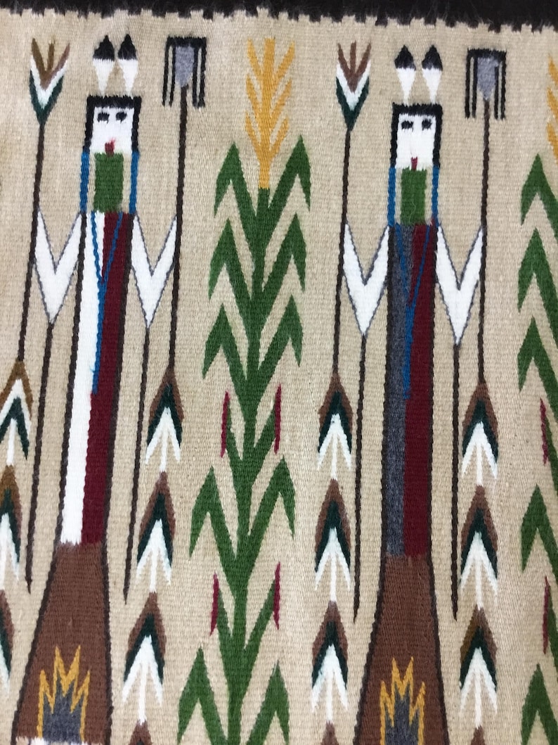 May include: A woven textile featuring a repeating pattern of stylized figures and plant motifs. The figures have white faces, green and blue accents, and hold spears. The background is tan, with green, yellow, and brown plant designs.