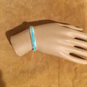 May include: A turquoise and silver bracelet with a geometric design. The bracelet is on a mannequin's wrist.