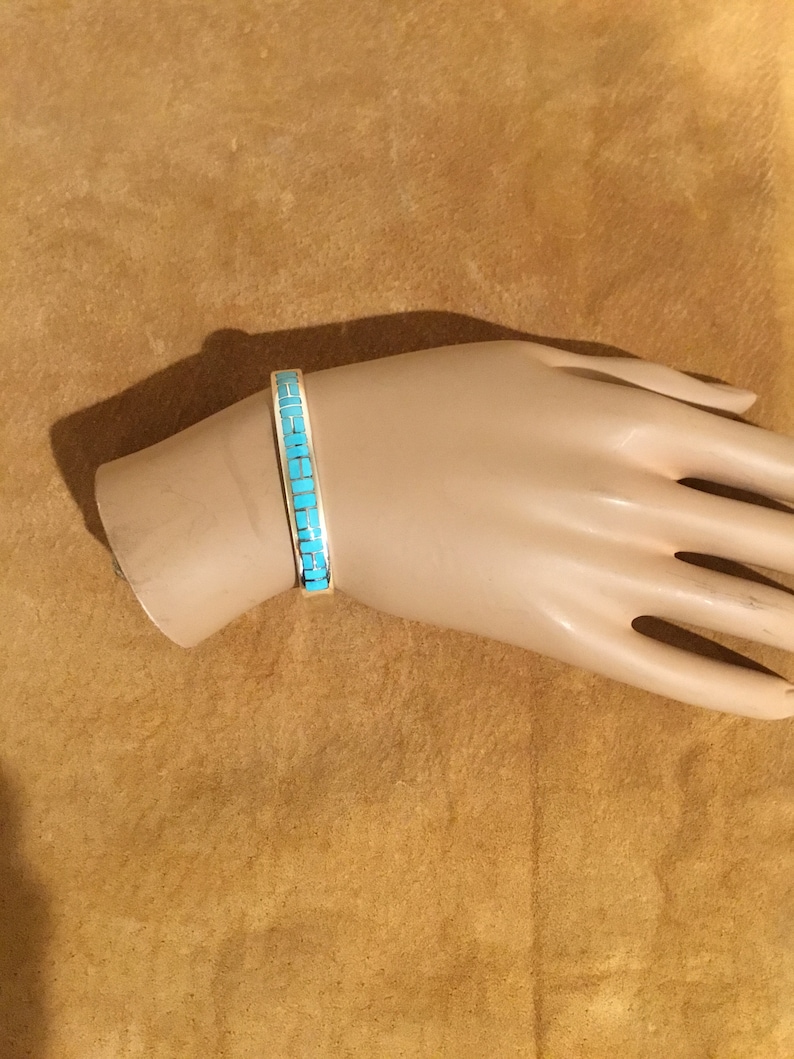 May include: A turquoise and silver bracelet with a geometric design. The bracelet is on a mannequin's wrist.