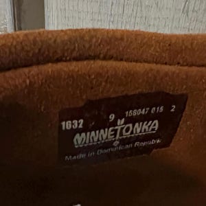 May include: Close-up of a brown leather boot interior. A rectangular label is visible with the brand name "MINNETONKA", size 9, and the number 1632. The label also indicates the boot was made in the Dominican Republic.