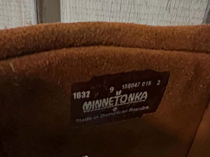 May include: Close-up of a brown leather boot interior. A rectangular label is visible with the brand name "MINNETONKA", size 9, and the number 1632. The label also indicates the boot was made in the Dominican Republic.
