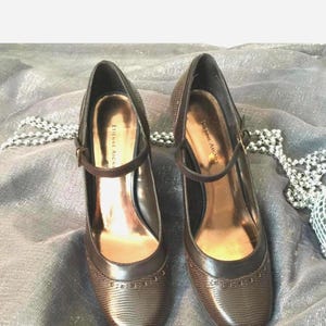 May include: A pair of brown leather shoes with a buckle strap. The shoes have a pointed toe and a low heel. The brand name "Etienne Aigner" is visible on the inside of the shoes.