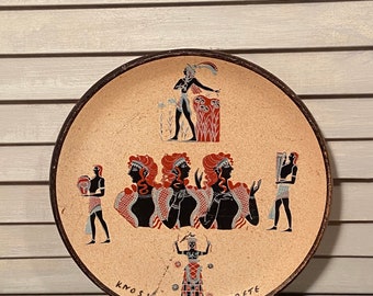 May include: A round ceramic plate with a brown rim and a beige background. The plate features a black and white illustration of a scene from ancient Greek mythology. The scene depicts a group of women in flowing robes, a man playing a lyre, and a woman holding a staff. The text "KNOSSOS CRETE" is written in black at the bottom of the plate.