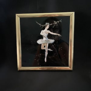 May include: A framed painting of a ballerina in a white tutu, with a black background and silver glitter accents.