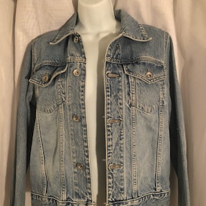 May include: A light blue denim jacket with a button closure and multiple pockets.