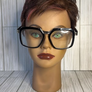 May include: A mannequin head with short brown hair with pink highlights wearing black and silver rectangular glasses.