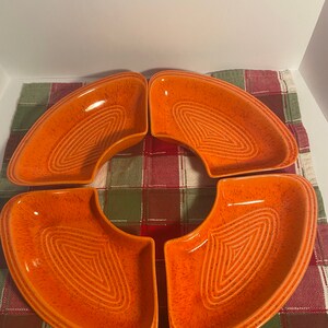 May include: Set of four orange ceramic serving dishes with a textured, speckled finish. The dishes are shaped like crescent moons and have a raised, concentric circle design in the center.
