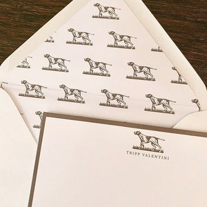 May include: A white envelope with a brown border and a repeating pattern of brown dogs. The envelope is folded in half and the inside is visible. The inside of the envelope has a white background with a brown dog illustration and the text "Tripp Valentini".