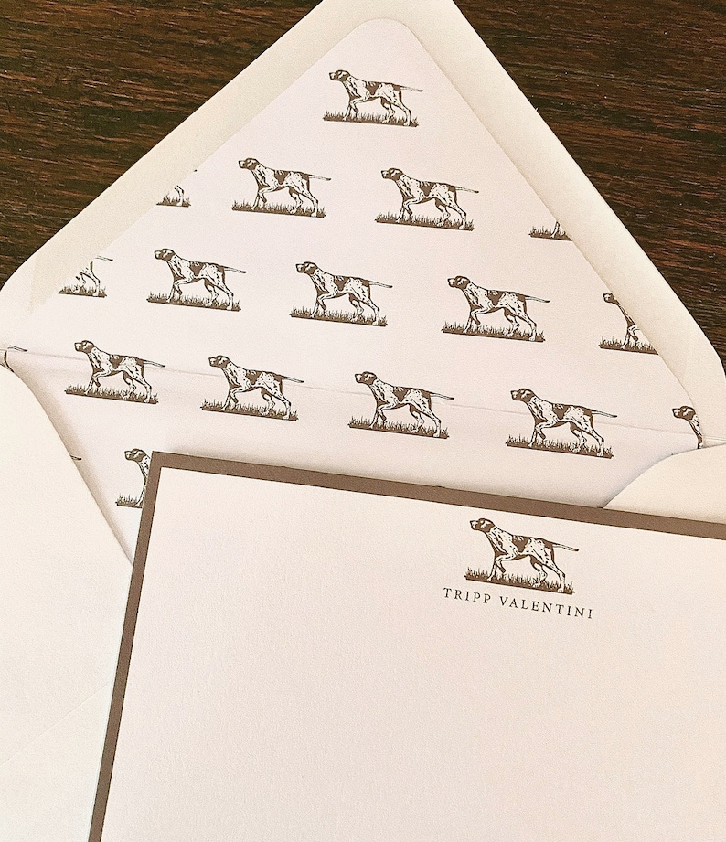 May include: A white envelope with a brown border and a repeating pattern of brown dogs. The envelope is folded in half and the inside is visible. The inside of the envelope has a white background with a brown dog illustration and the text "Tripp Valentini".