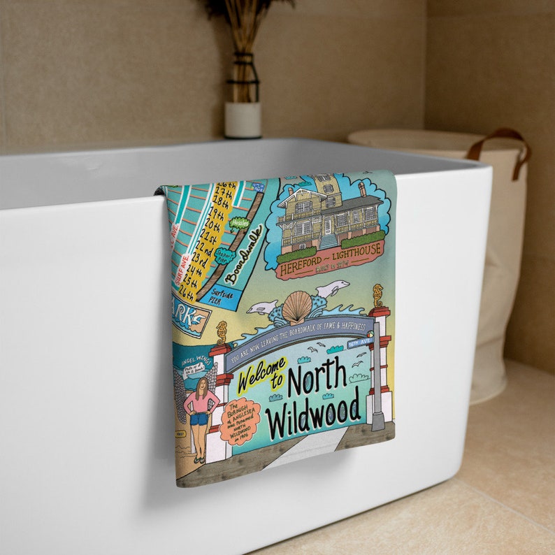 May include: A colorful illustration of a beach town with the words "Welcome to North Wildwood" on a towel. The illustration includes a lighthouse, boardwalk, and beach.