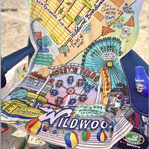 May include: A colourful beach towel featuring a map of Wildwood, New Jersey. The towel depicts a Ferris wheel, a boardwalk, and the text "2 miles of smiles".