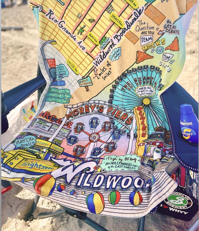 May include: A colourful beach towel featuring a map of Wildwood, New Jersey. The towel depicts a Ferris wheel, a boardwalk, and the text "2 miles of smiles".