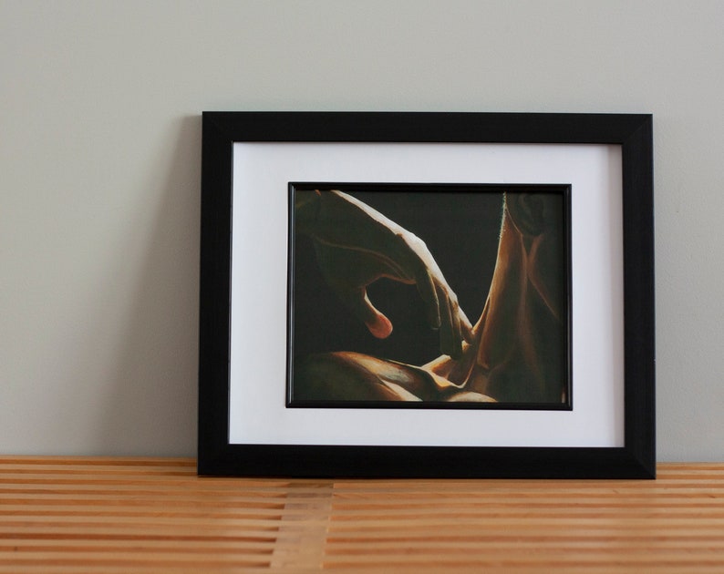 May include: A framed print of a painting depicting two hands intertwined, with one hand reaching out towards the other. The hands are illuminated by a warm, golden light, while the background is dark and shadowy.