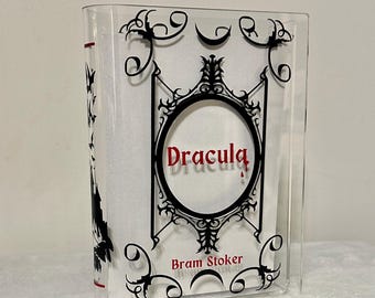May include: A clear acrylic bookend with a black and white design featuring a gothic-style frame with the title "Dracula" and the author "Bram Stoker" printed in white.