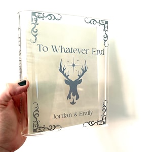 May include: Clear acrylic block with the text "To Whatever End" and the silhouette of a stag with a starburst. The names "Jordan & Emily" are printed below the stag. Decorative gray corner accents frame the text.
