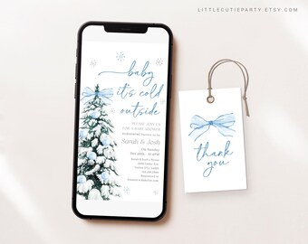 May include: A baby shower invitation on a smartphone screen with a matching tag. The invitation features a snowy Christmas tree and the text "baby it's cold outside." The tag says "thank you" with a blue bow.