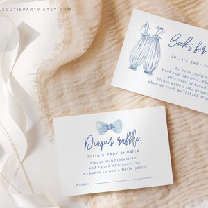 K&ouml;nnte beinhalten: Zwei blaue und wei&szlig;e Babyparty-Karten. Eine Karte sagt "B&uuml;cher f&uuml;r Baby" und hat eine Aquarell-Illustration einer Baby-Latzhose. Die andere Karte sagt "Windel-Tombola" und hat eine Aquarell-Illustration einer blauen Fliege.