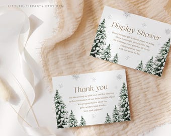 Peut inclure: Deux cartes blanches avec du texte et des illustrations pour une baby shower. Les cartes ont un thème hivernal avec des pins verts et des flocons de neige. Une carte dit "Display Shower" et l'autre dit "Thank you".