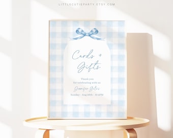May include: A blue and white gingham card and gift sign with a blue bow. The sign says "Cards + Gifts" and includes the text "Thank you for celebrating with us Jennifer Gates Sunday, Aug 26th - At 2PM".