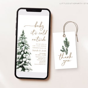 May include: A smartphone displays a baby shower invitation with the text "baby it's cold outside." A snow-covered evergreen tree is on the left. A matching tag with "thank you" is on the right.