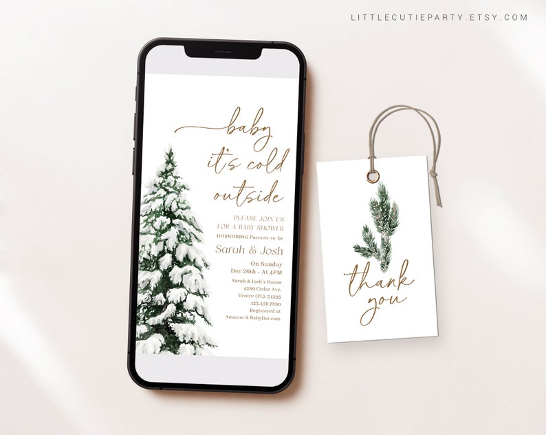 May include: A smartphone displays a baby shower invitation with the text "baby it's cold outside." A snow-covered evergreen tree is on the left. A matching tag with "thank you" is on the right.