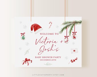 May include: A white sign with red text and watercolor illustrations for a baby shower. The sign says "Welcome to Victoria + Josh's Baby Shower Party December 26th." Christmas-themed illustrations include a Santa hat, ornaments, and a gift.
