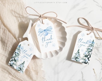 Könnte beinhalten: Weiße Geschenkanhänger mit Winterthema. Jeder Anhänger zeigt ein Aquarelldesign einer blauen Schleife, Schneeflocken oder schneebedeckten Kiefern, mit den Worten "Danke" in blauer Schrift. Die Anhänger sind mit einer beigen Schnur gebunden.
