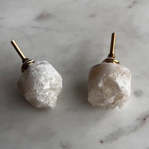 May include: Two white crystal cabinet knobs with gold metal bases. The crystal is rough and has a natural, organic look.
