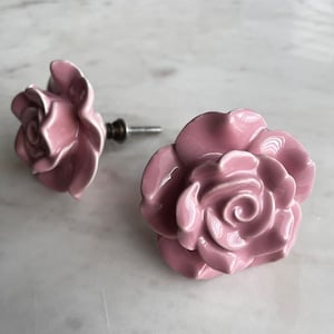 May include: Two pink ceramic rose-shaped drawer pulls with a silver metal screw.