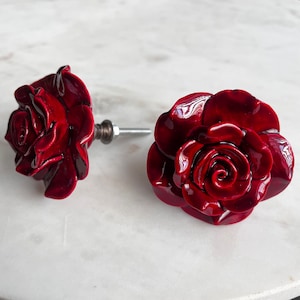 May include: Two red ceramic rose-shaped drawer pulls with a silver metal stem.