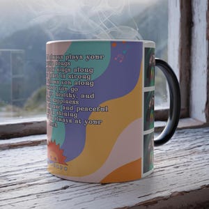 Puede incluir: Una taza de cerámica con asa negra, con un diseño colorido con texto y un gráfico de sol. La taza tiene un diseño con colores pastel y una cita. La taza está sobre una superficie de madera.