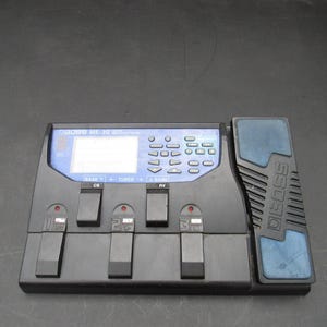 May include: A black Boss ME-30 guitar multi-effects processor featuring a central digital display, a blue control panel with various buttons, three numbered foot switches, two additional control switches, and a large integrated expression pedal.