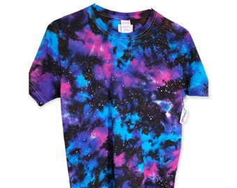 Puede incluir: Una camiseta negra con un patrón de tie-dye de galaxia en tonos de azul, rosa y morado. La camiseta tiene cuello redondo y mangas cortas.