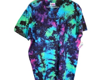 May include: A black t-shirt with a tie-dye pattern in shades of blue, green, and pink. The shirt has a galaxy-like design with white speckles throughout.