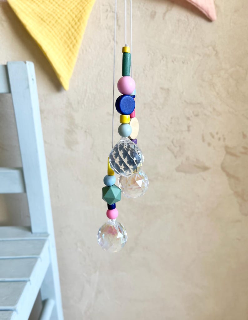 Peut inclure: Un attrape-soleil en cristal avec une cha&icirc;ne de perles en bois color&eacute;es. Les perles sont dans des tons de rose, bleu, vert, jaune et blanc.