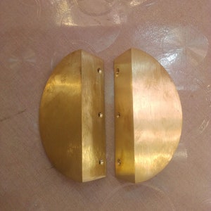 May include: Two gold-colored metal door handles, each shaped like a half-circle, with a flat back and four small holes.