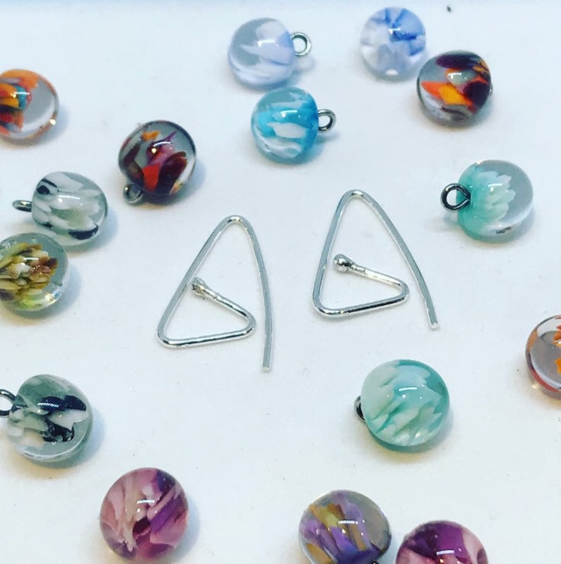 Puede incluir: Un par de ganchos para pendientes de plata en forma de tri&aacute;ngulo con una peque&ntilde;a bola en la parte superior. Los pendientes est&aacute;n rodeados de una variedad de cuentas de vidrio de colores con patrones abstractos.
