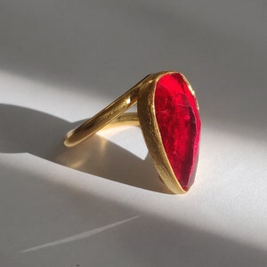 Peut inclure: Une bague en or avec une grande pierre rouge en forme de larme.