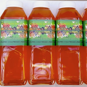 Puede incluir: Varias botellas de pl&aacute;stico transparente llenas de l&iacute;quido naranja, cada una con una tapa blanca. Las botellas tienen etiquetas verdes con el texto "PUMPKIN SEED OIL GARDEN OF ESSENCE EXTRA VIRGIN". Las etiquetas tambi&eacute;n incluyen el texto "ORGANIC COLD PRESSED UNREFINED".