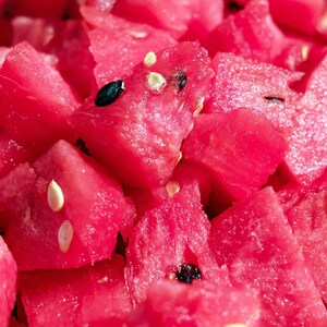 May include: Close-up of a pile of fresh, diced watermelon. The bright red fruit is cut into irregular chunks, with visible black and white seeds. The image highlights the juicy texture and vibrant color of the watermelon.