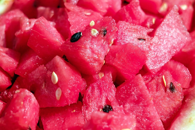 May include: Close-up of a pile of fresh, diced watermelon. The bright red fruit is cut into irregular chunks, with visible black and white seeds. The image highlights the juicy texture and vibrant color of the watermelon.