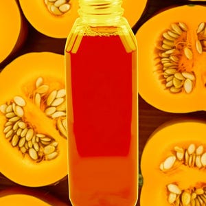 May include: A clear plastic bottle filled with orange-red liquid, likely juice or a beverage, is centered in the image. The bottle is surrounded by halved pumpkins, showcasing the orange flesh and seeds. The background is a wooden surface.