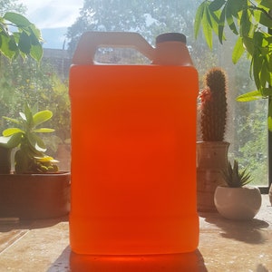 May include: A large, orange-colored plastic jug with a white handle and a black cap. The jug is filled with a bright orange liquid.